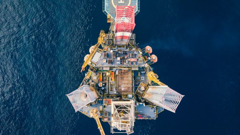 Aerial top-down view of an offshore drilling rig with helipad in deep blue sea, illustrating ADNOC Drilling's record Q2 2026 and $262.5 million dividend