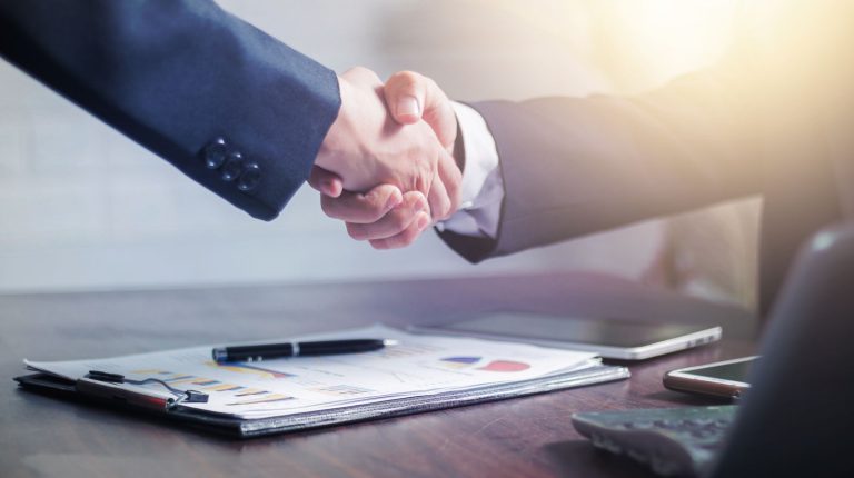 Business handshake over deal documents, symbolising M&A transactions subject to UAE merger control from 30 July 2026