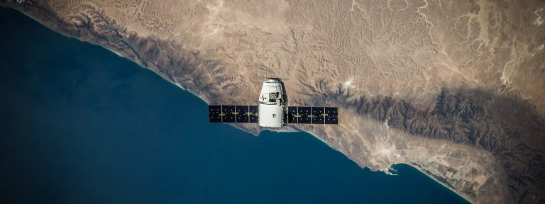 Satellite with solar panels orbiting above a desert coastline, symbol of UAE-built Earth observation technology