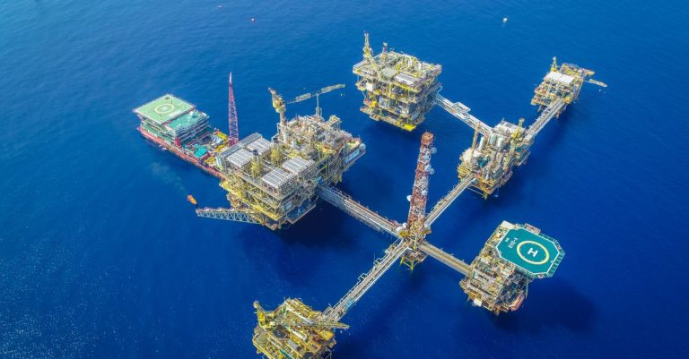 Aerial view of an offshore gas platform complex in deep blue ocean waters, illustrating XRG and bp equal stakes in the Loran gas licence near Trinidad and Tobago