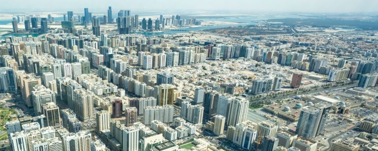 Aerial view of Abu Dhabi with dense blocks of high-rise buildings and island towers on the horizon