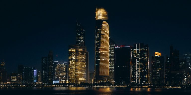 Abu Dhabi skyline at night seen across the water, with illuminated towers along the Corniche, the emirate where Pantheon opened its first office in ADGM