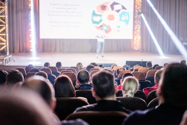 Full conference hall with a speaker on stage and a presentation screen during a technology summit