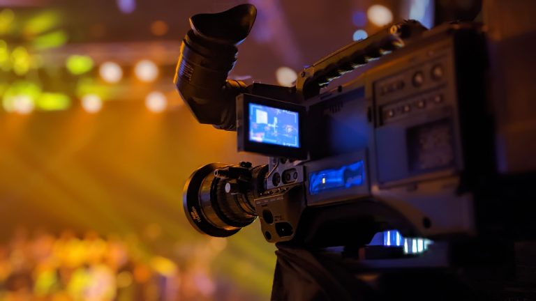 Professional broadcast camera on a tripod filming a lit stage at a media event, illustrating the 24th Arab Media Summit at Dubai World Trade Centre from 15 to 17 September 2026