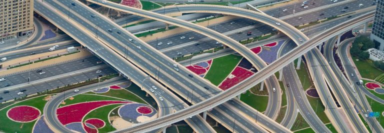 Aerial view of a multi level highway interchange in Dubai with elevated bridges, a rail viaduct and wide multi lane carriageways, illustrating the new 80 km Fourth Corridor