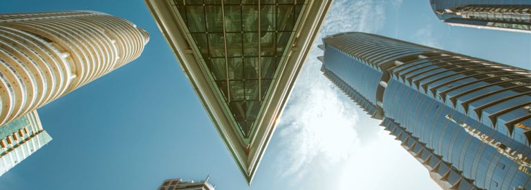 Low angle view of glass skyscrapers and a triangular glass canopy against a blue sky in Dubai