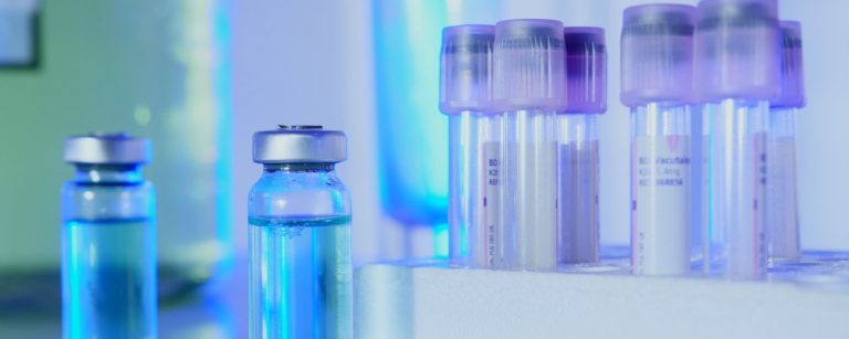 Glass vials with blue liquid and blood sample tubes in a rack in a laboratory under blue light