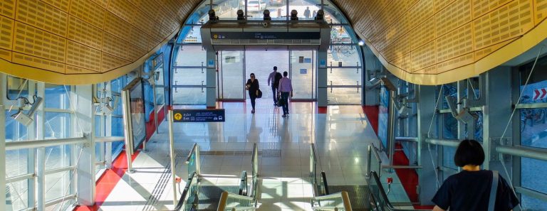 Commuters walk towards the Sheikh Zayed Road exit of a sunlit Dubai Metro station above the escalators