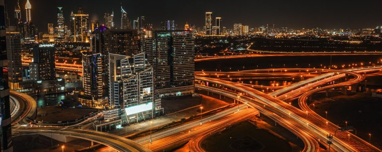 Dubai at night with light trails on a multi-level highway interchange and illuminated towers on the skyline