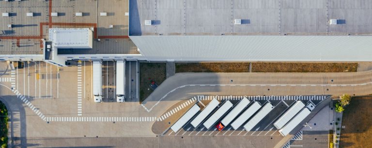 Aerial view of a large logistics warehouse with truck loading docks and parked semi-trailers