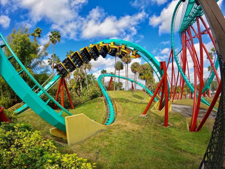 Roller coaster train in an inversion above palm trees at a theme park under a blue sky, illustrating the Miral plan to invest more than AED 12 billion in new rides and park expansions on Yas Island