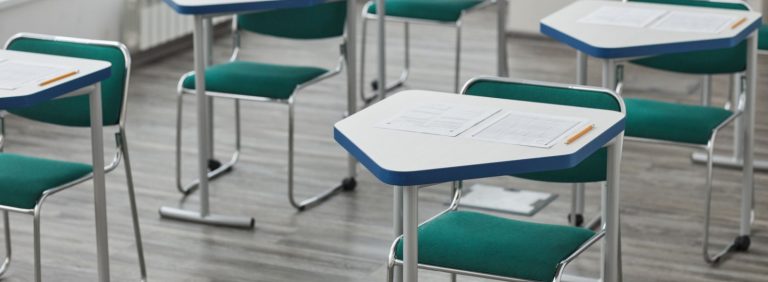 Empty exam room with desks, answer sheets and pencils laid out before a test, illustrating UAE Cabinet Resolution No. 143 of 2026 on violations and penalties for universities and exam integrity