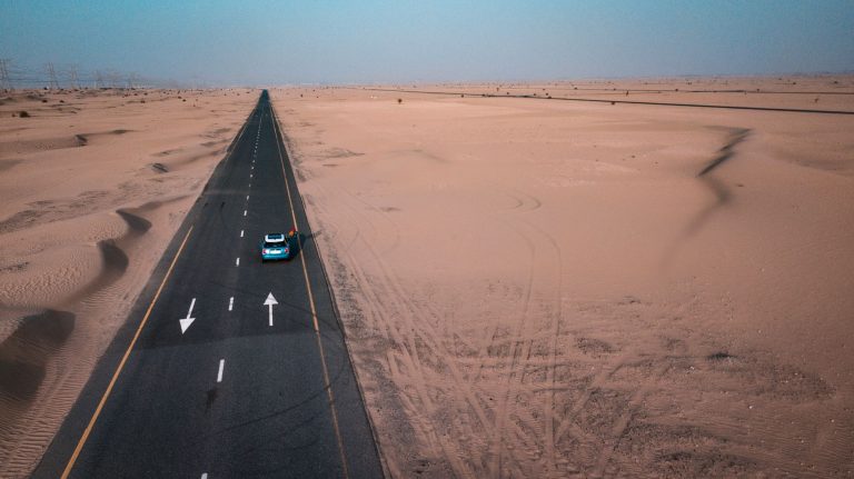 Aerial view of an empty desert highway crossing sand dunes in the UAE with a single car on the road