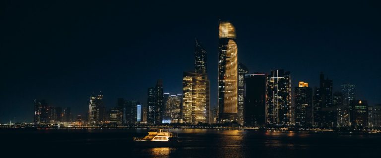 Abu Dhabi Corniche skyline at night with lit towers over the water, illustrating the Apollo investment in Mubadala Capital