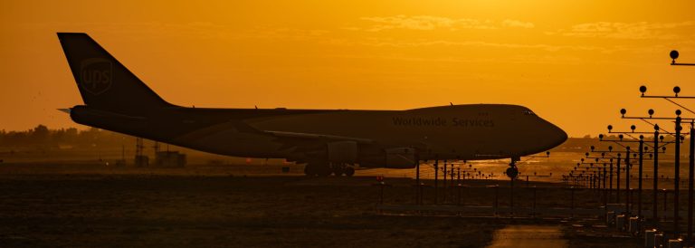 Silhouette of a Boeing 747 freighter on an airport runway against an orange sunset sky