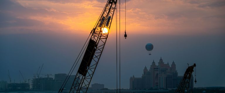 Construction cranes at sunset with Atlantis The Palm on the skyline, illustrating AED 2.1 trillion of projects under way in Dubai