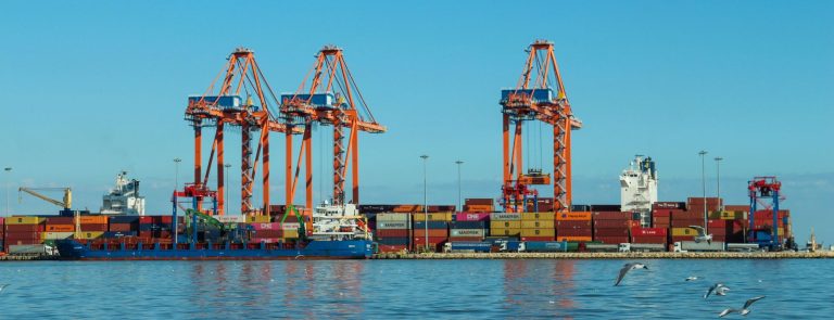 Container terminal with orange gantry cranes, stacked containers and a cargo ship, illustrating Dubai-China trade
