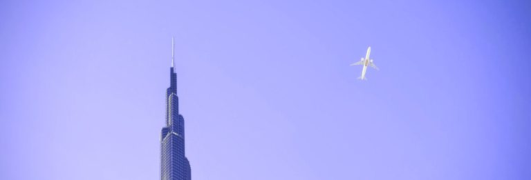 A passenger airliner flying past the spire of Burj Khalifa in Dubai against a clear sky