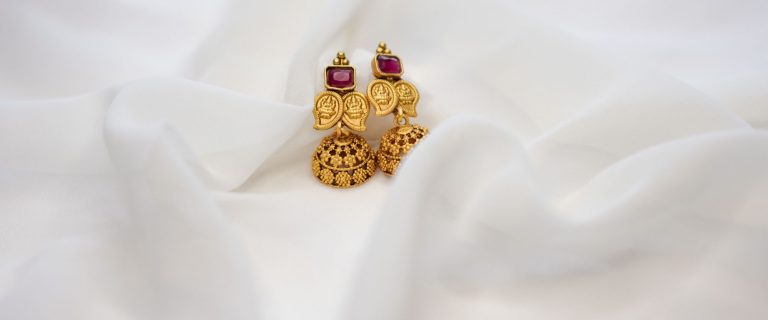 Pair of traditional gold jhumka earrings with red stones on white fabric