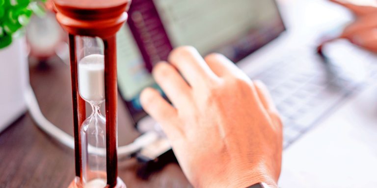 Hourglass next to a hand typing on a laptop, illustrating the 60-minute business account opening launched by RAKEZ and Rakbank