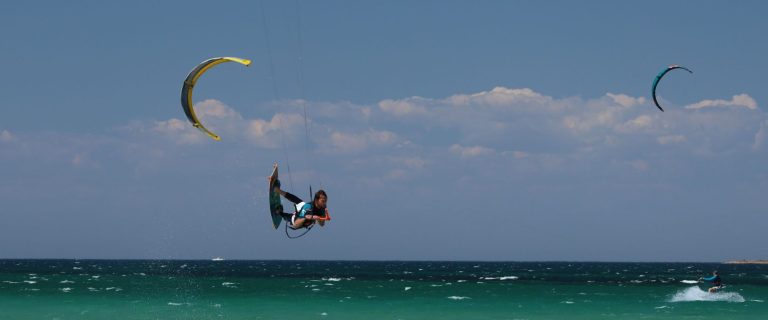 Kiteboarder in mid-air holding the control bar under a yellow kite above a turquoise sea
