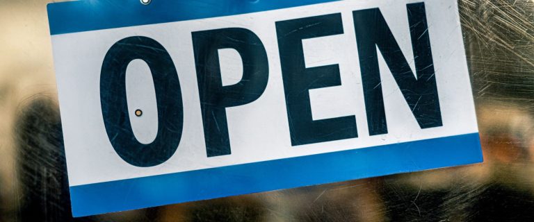 Blue and white OPEN sign hanging on a shop glass door, illustrating growth in new business licences in Ras Al Khaimah