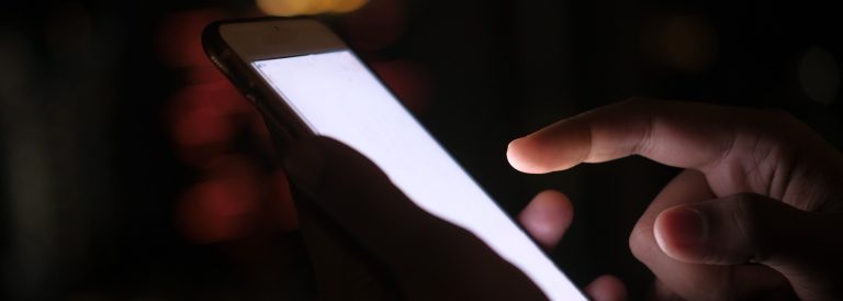 Hand using a smartphone app at night with blurred city lights behind