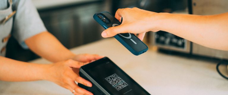 Customer scans a QR code on a merchant payment terminal with a smartphone, illustrating digital payments and e-wallets in the UAE