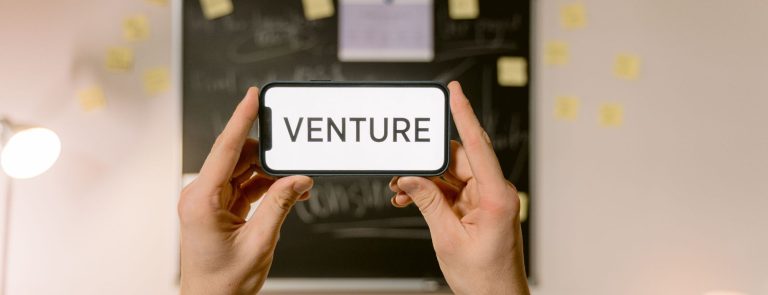 Hands holding a smartphone with the word VENTURE on screen, illustrating venture funding for UAE startups