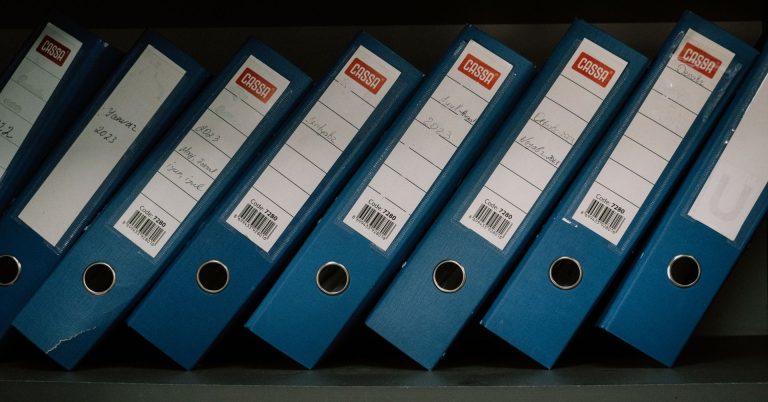 Blue office binders on a dark shelf, illustrating AML record keeping and compliance files for UAE DNFBPs